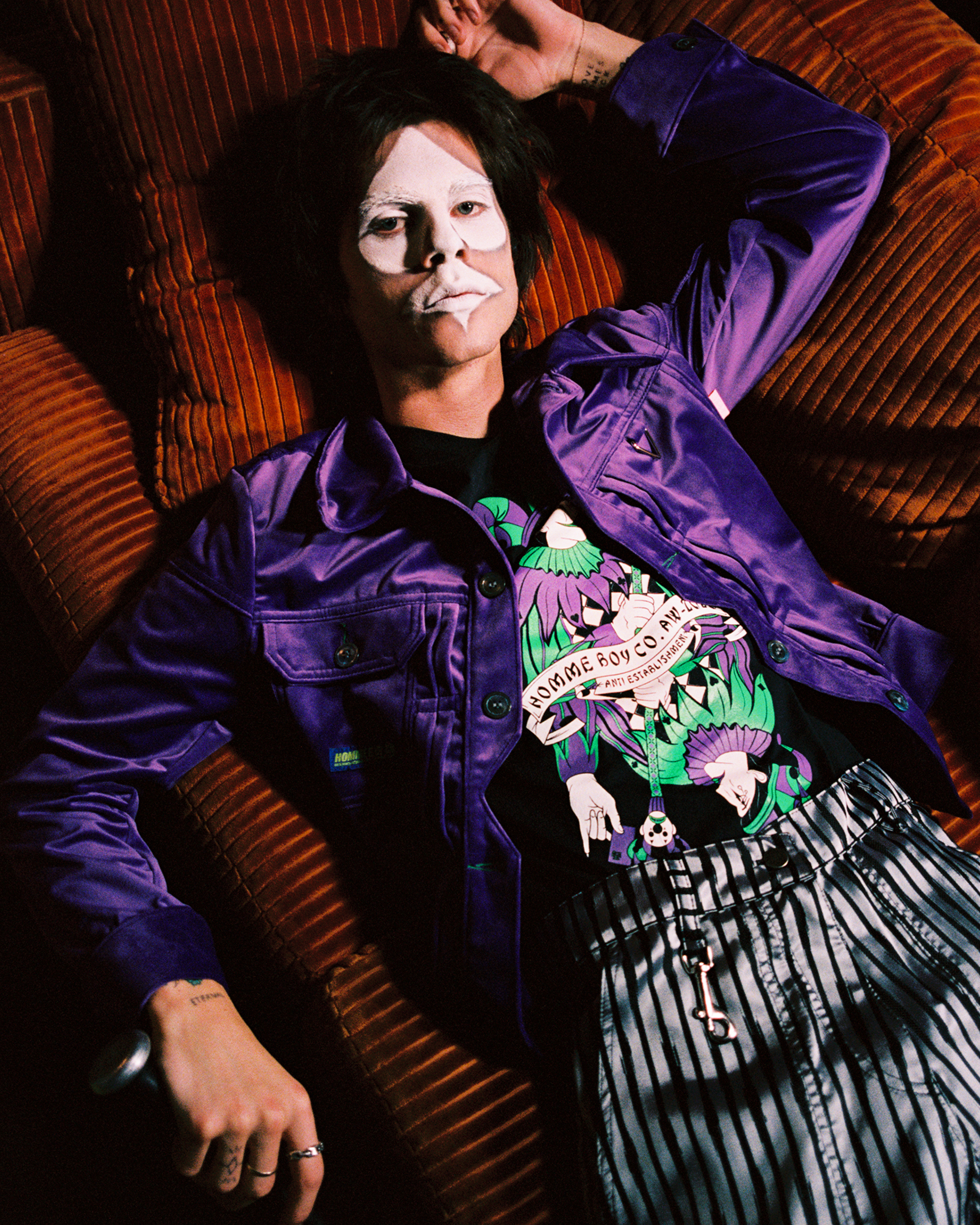 Model laying on a red couch with white spade shaped facepaint